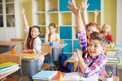 Happy kids in classroom raising their hands because they know the answer_reduced